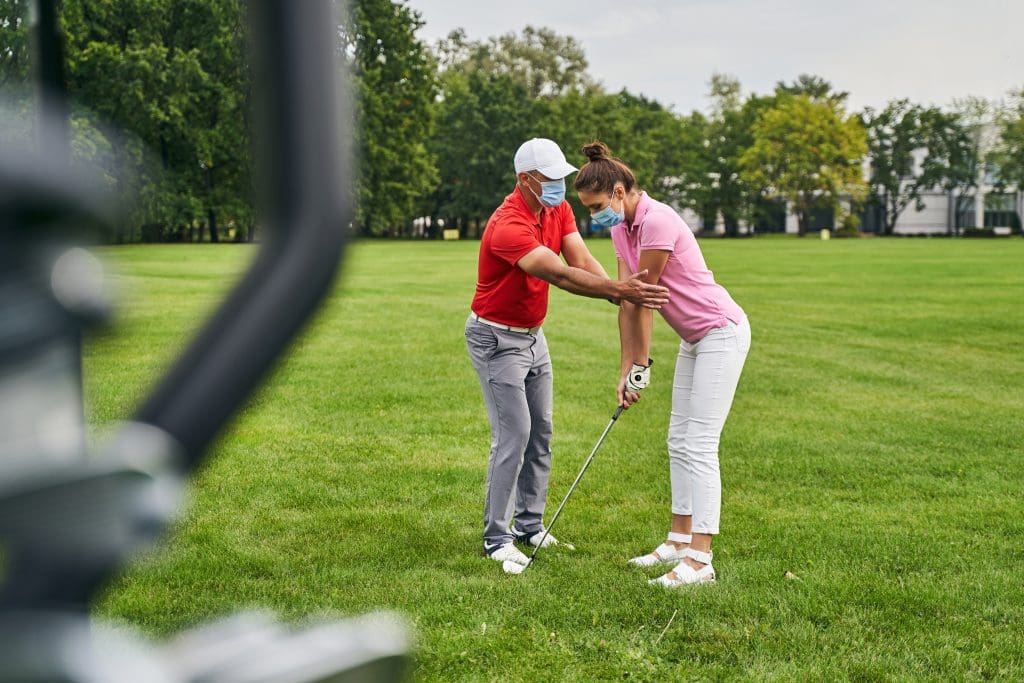 Mujer enfocada golfista aprendiendo a colocar la postura adecuada asistida por su entrenador personal